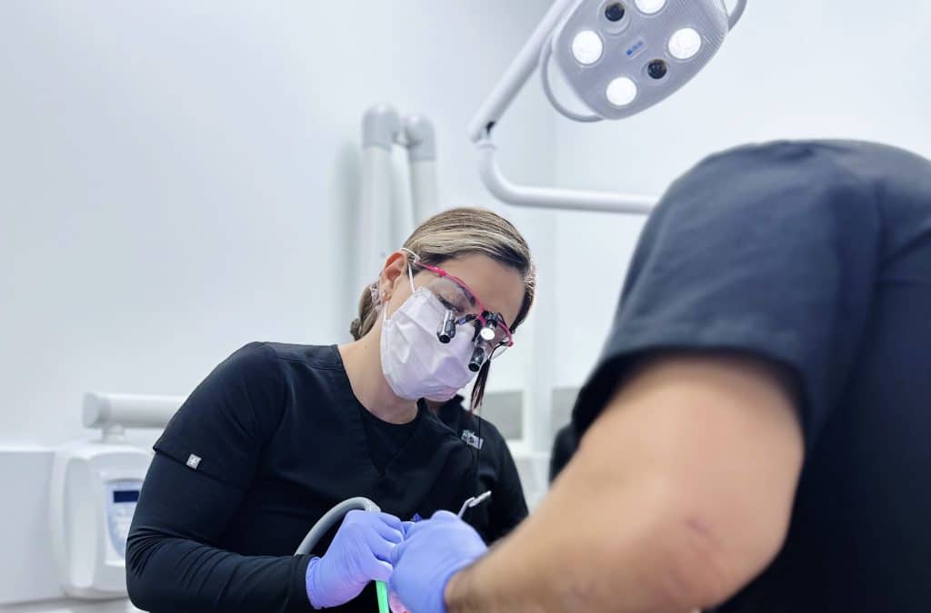 Dentista realizando tratamiento de conducto en paciente, con equipo dental y luz de consulta en un ambiente clínico moderno.