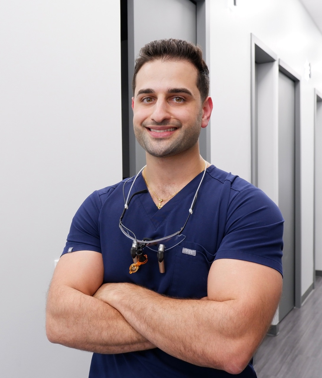 Dr. Bobby Yasso, dentist at Ultra Dental, wearing a blue scrub and dental loupes, smiling confidently in a modern dental office setting.